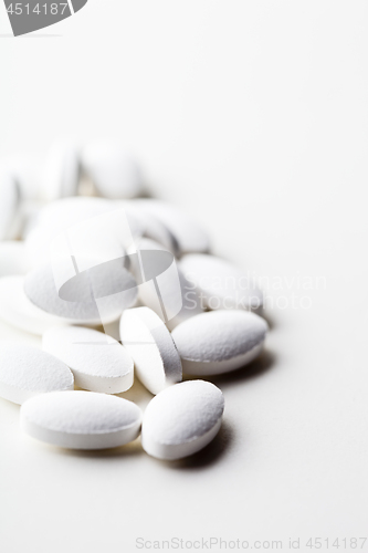 Image of Pile of white drug pills laying on white background.
