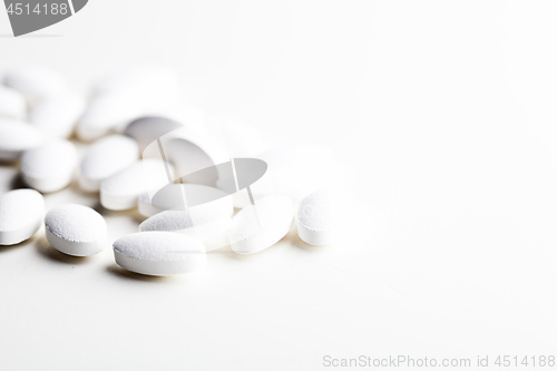 Image of Pile of white drug pills laying on white background.