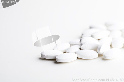 Image of Pile of white drug pills laying on white background.