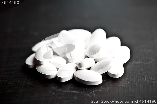 Image of Pile of white drug pills laying on black board background.