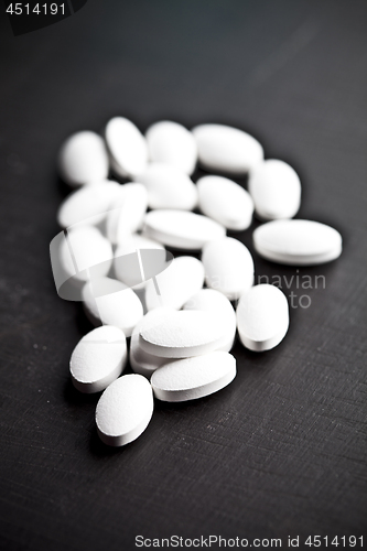 Image of Pile of white drug pills laying on black board background.