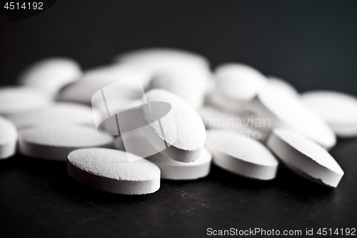 Image of Pile of white drug pills laying on black board background.