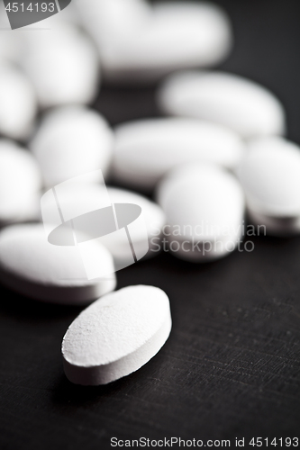 Image of Pile of white drug pills laying on black board background.