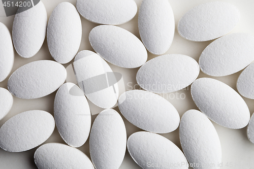 Image of Pile of white drug pills laying on white background.