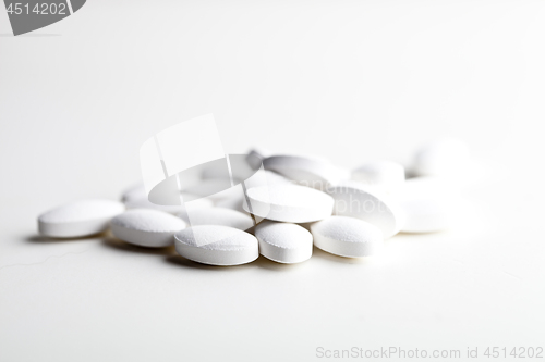 Image of Pile of white drug pills laying on white background.