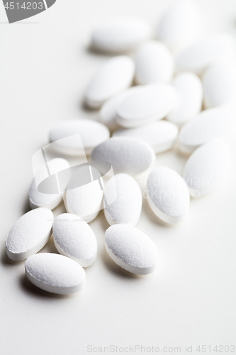 Image of Pile of white drug pills laying on white background.