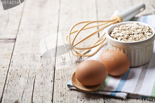 Image of Fresh chicken eggs, oat flakes in ceramic bowl and kitchen utens