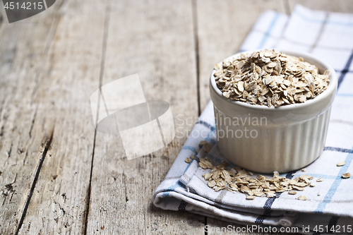 Image of Oat flakes in ceramic bowl on linen napkin, golden wheat ears on