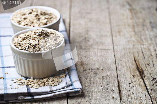 Image of Oat flakes in ceramic bowls on linen napkin, golden wheat ears o