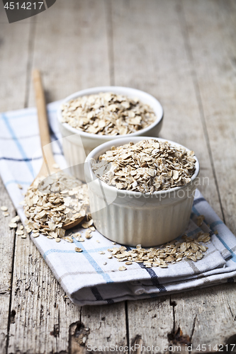 Image of Oat flakes in ceramic bowls and wooden spoon, golden wheat ears 