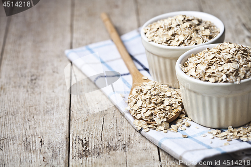 Image of Oat flakes in ceramic bowls and wooden spoon on linen napkin, go