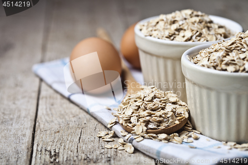 Image of Fresh chicken eggs, oat flakes in ceramic bowl and wooden spoon 