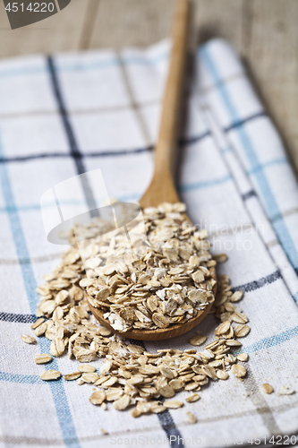 Image of Oat flakes in wooden spoon on linen napkin, golden wheat ears on