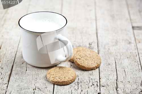 Image of Cup of milk and some fresh baked oat cookies on rustic wooden ta