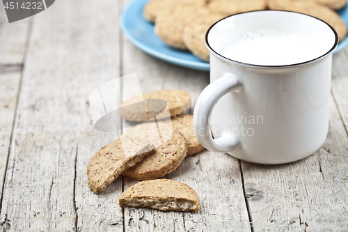 Image of Cup of milk and fresh baked oat cookies on blue ceramic plate on