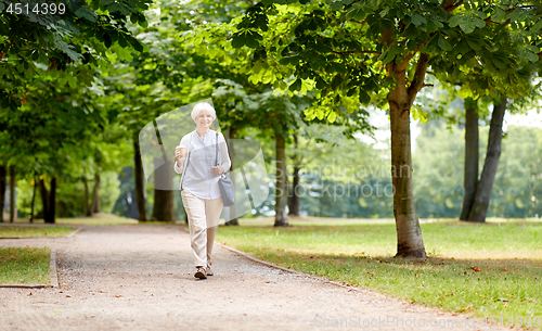 Image of senior woman walking with takeaway coffee at park