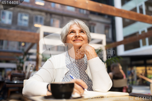 Image of senior woman with notebook dreaming at street cafe