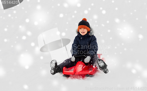 Image of happy boy sliding on sled down snow hill in winter