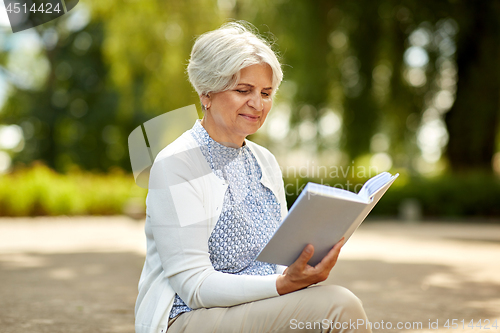 Image of senior woman reading book at summer park