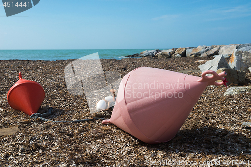 Image of Two big buoys on the beach, azure sea and the rocky beach