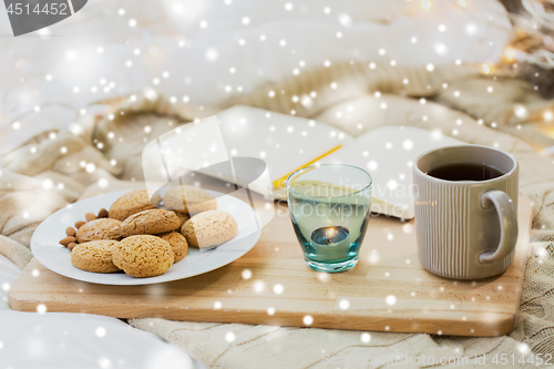 Image of cookies, tea and candle at home over snow