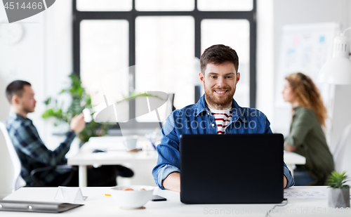 Image of smiling creative man with laptop working at office