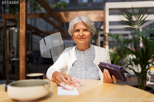 Image of senior woman with money paying bill at cafe