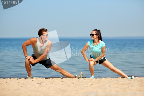 Image of smiling couple stretching legs on beach