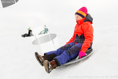 Image of happy kids sliding on sled down hill in winter