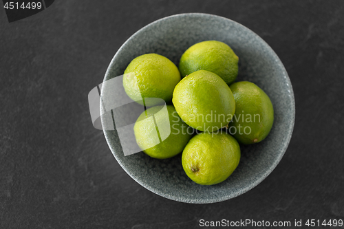 Image of close up of whole limes in bowl on slate table top