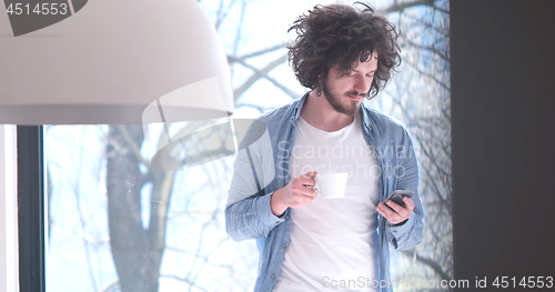 Image of young man drinking coffee and using a mobile phone  at home