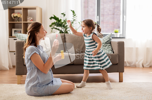 Image of pregnant mother and daughter blowing soap bubbles