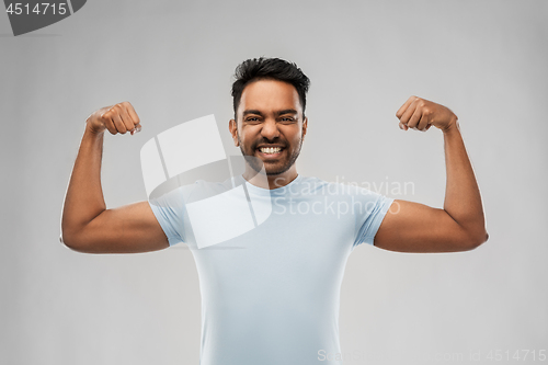 Image of indian man showing biceps over grey background