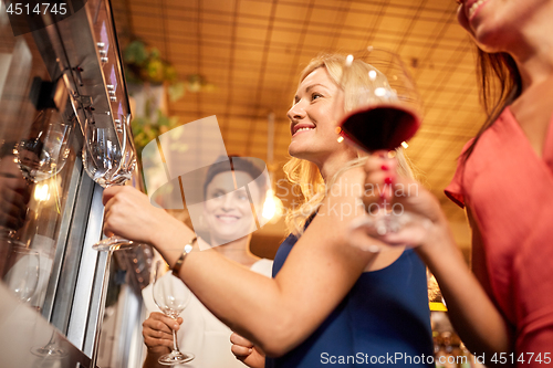 Image of happy women pouring wine from dispenser at bar