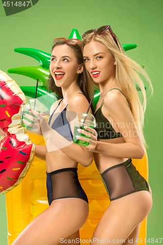 Image of Cute girls in swimsuits posing at studio. Summer portrait caucasian teenagers on green background.