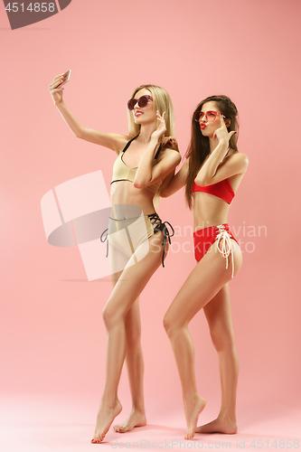 Image of Cute girls in swimsuits posing at studio. Summer portrait caucasian teenagers on pink background.