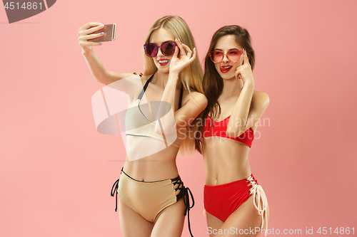 Image of Cute girls in swimsuits posing at studio. Summer portrait caucasian teenagers on pink background.