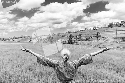 Image of Relaxed fashionable caucasian woman wearing asian style kimono, arms rised to sky, enjoying pure nature at beautiful green rice fields on Bali island