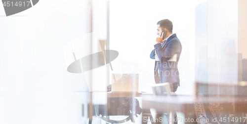 Image of Businessman talking on a mobile phone in corporate office while looking through window.