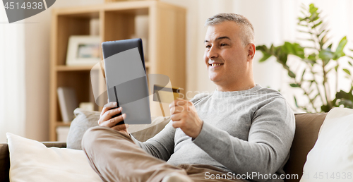 Image of man with tablet pc and credit card on sofa at home