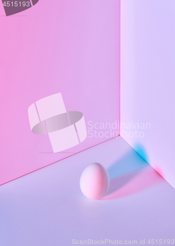 Image of Multi-colored egg on a double pink-lilac background with a reflection of blue-pink shadows and copy space for text. Easter layout