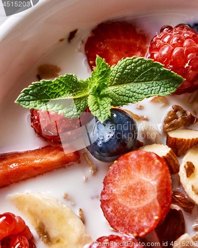 Image of Fresh milk with homemade honey granola and natural organic ingredients - berries, nuts and mint in the white ceramic bowl. Close-up.