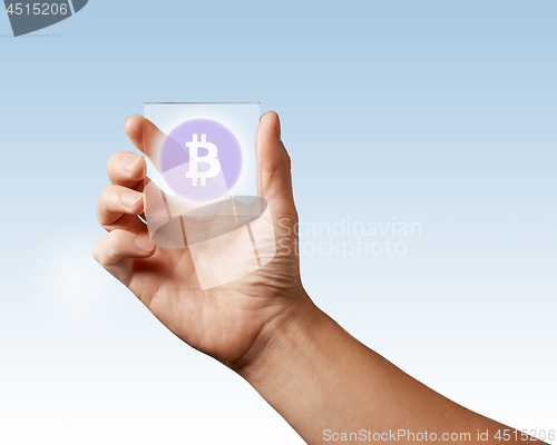 Image of A man\'s hand holds a transparent digital screen with a bitcoin icon ns blue background