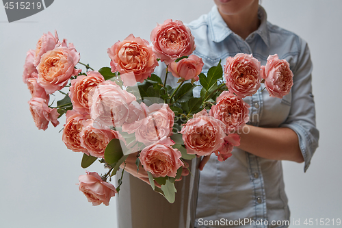 Image of A bouquet of fresh pink roses in a brown vase holds a girl in her hands