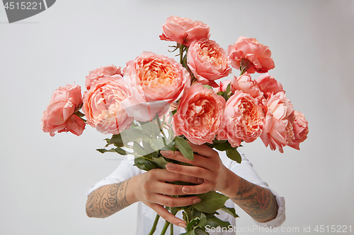 Image of Young girl\'s hands is holding a bouquet of fresh flowers in her hands with tatoo in a color of the year 2019 Living Coral Pantone