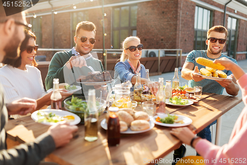 Image of happy friends eating at barbecue party on rooftop