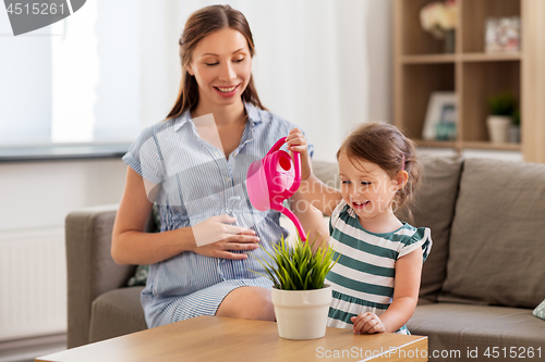 Image of pregnant mother and daughter watering home plant