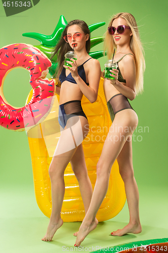 Image of Cute girls in swimsuits posing at studio. Summer portrait caucasian teenagers on green background.