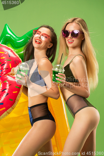 Image of Cute girls in swimsuits posing at studio. Summer portrait caucasian teenagers on green background.