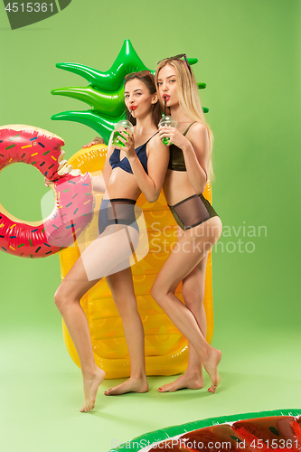 Image of Cute girls in swimsuits posing at studio. Summer portrait caucasian teenagers on green background.